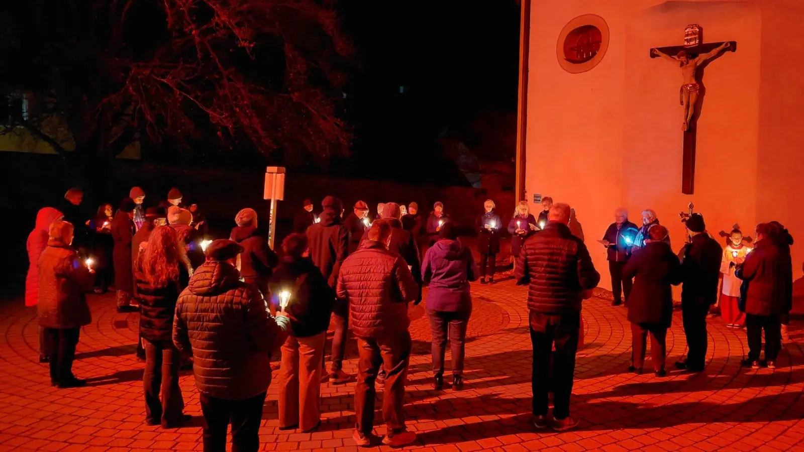 Die Teilnehmer beteten bei der 3. Station des „Pilgerweges der Hoffnung” am Kirchplatz vor der Rot beleuchteten Pfarrkirche St. Martin. (Bild: Georg Hirsch)