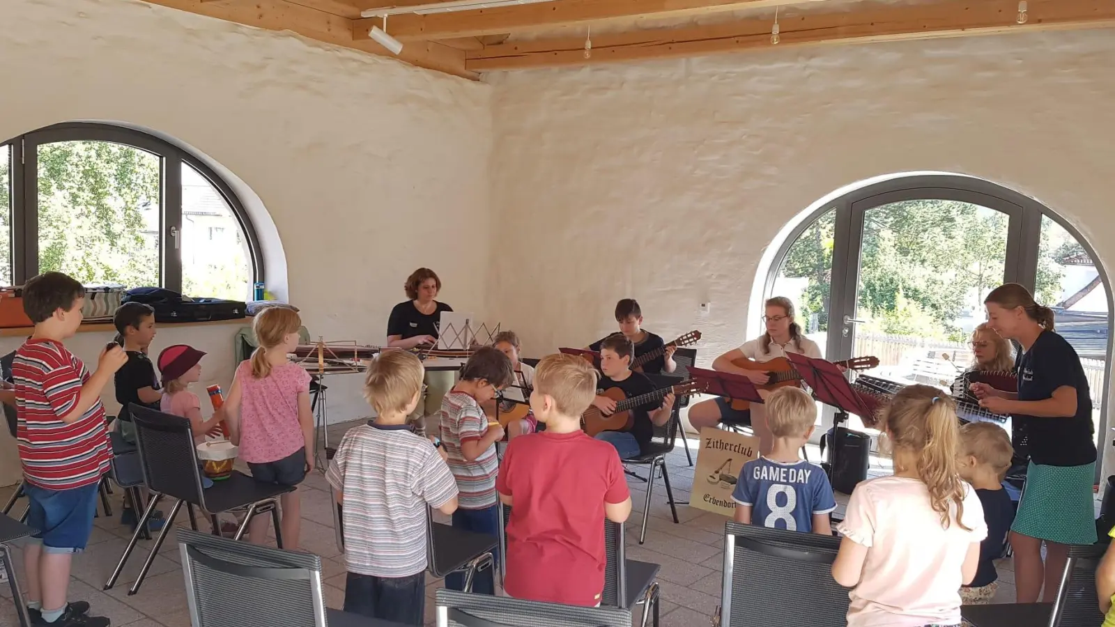 Unter der Leitung von Dirigentin Veronika Hille (rechts hinten stehend) musizierten die Zitherclubmusikanten. Kinder begleiteten rhythmisch mit Rasseln und Trommeln. (Bild: Heidi Banzer)