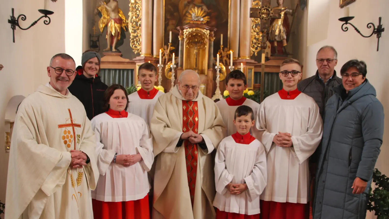 Jubilar P. Friedhelm Czinczoll gemeinsam mit Pfr. Thomas Vogl, sowie in der Ministrantenschar neu aufgenommenen Ministrant Thomas Ernst. Ebenso gratulierten den Beiden die Oberministranten Josepha Wifling und Lukas Wurm, Ministranten Ferdinand Hausner, Lena Kraus und Matthias Forster, wie auch Kirchenpfleger Gerhard Ernstberger mit PGR-Sprecherin Bettina Männer. (Bild: Lukas Forster)