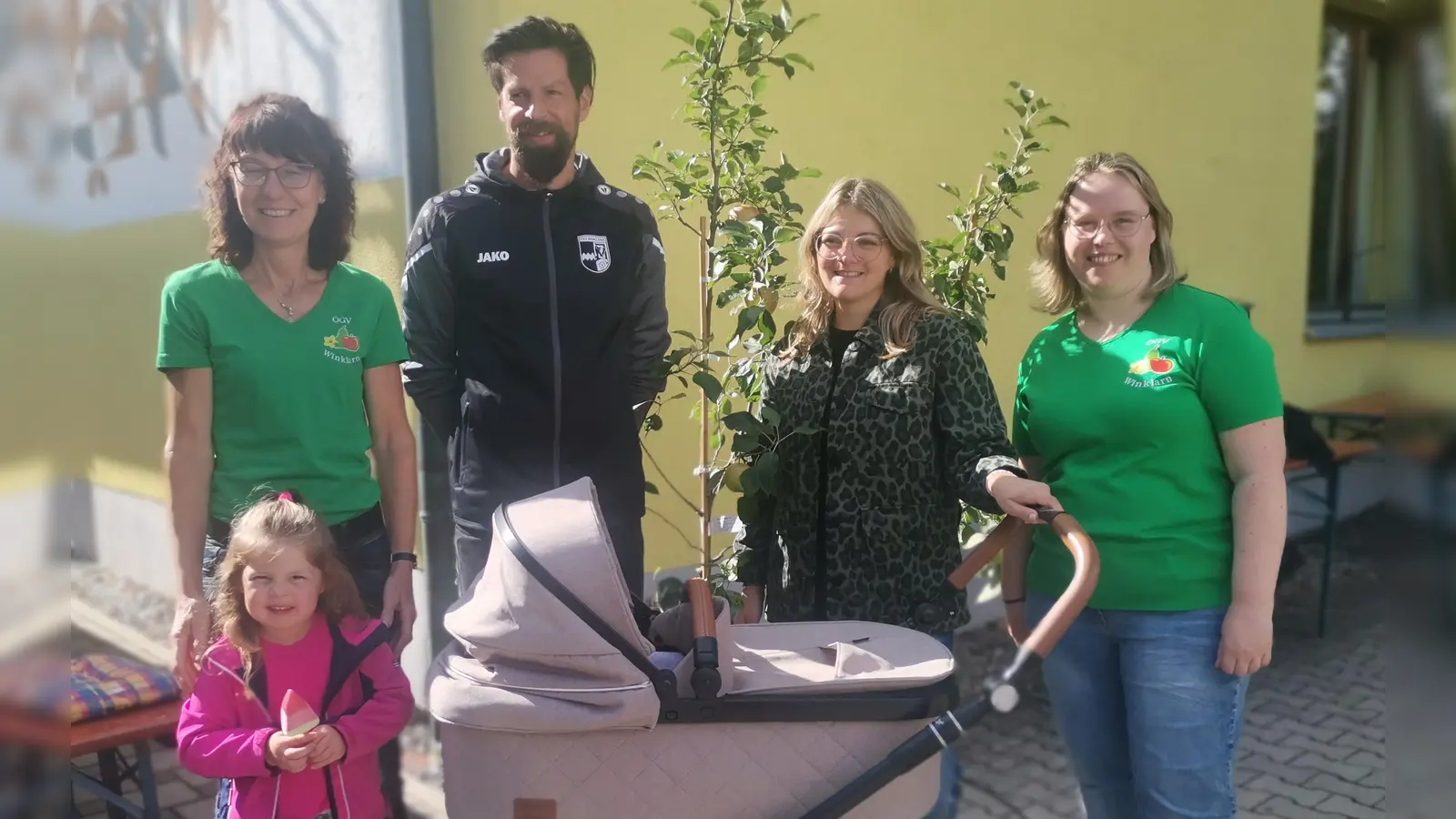 Anita Dietl (links) und Nicole Spachtholz (rechts) übergeben den Apfelbaum an Familie Hutzler für ihre Tochter Tessa. (Bild: Annemarie Mösbauer)