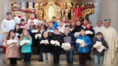 Die Erstkommunionkinder, die in den Händen ihre Albe halten, mit Ministranten, Pfarrer Helmut Brügel und Pastoralreferent Stefan Dotzler. (Bild: Anita Hartmann)