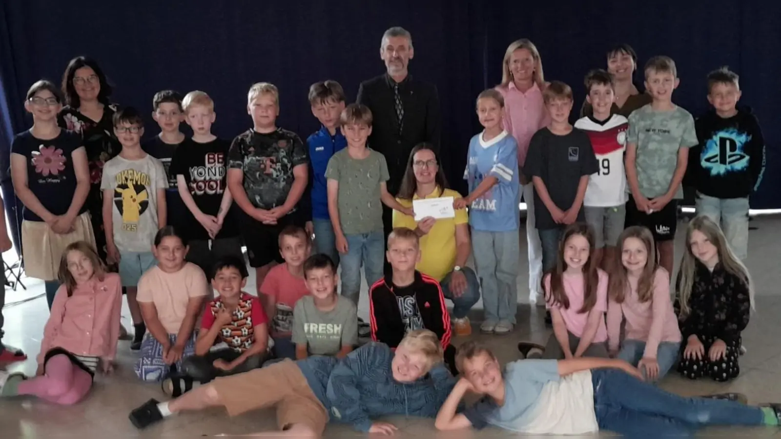 Bildunterschrift: Kommunionkinder der Pfarreiengemeinschaft – mit Christine Hecht von FLIKA – Bildmitte: Pfarrer Helmut Brügel, rechts daneben: Konrektorin Sabine Spindler, links hinten: Klassleiterin Julia Wendl-Schön, rechts neben Konrektorin Spindler: Klassleiterin Alexandra Erren (Bild: Helmut Brügel)