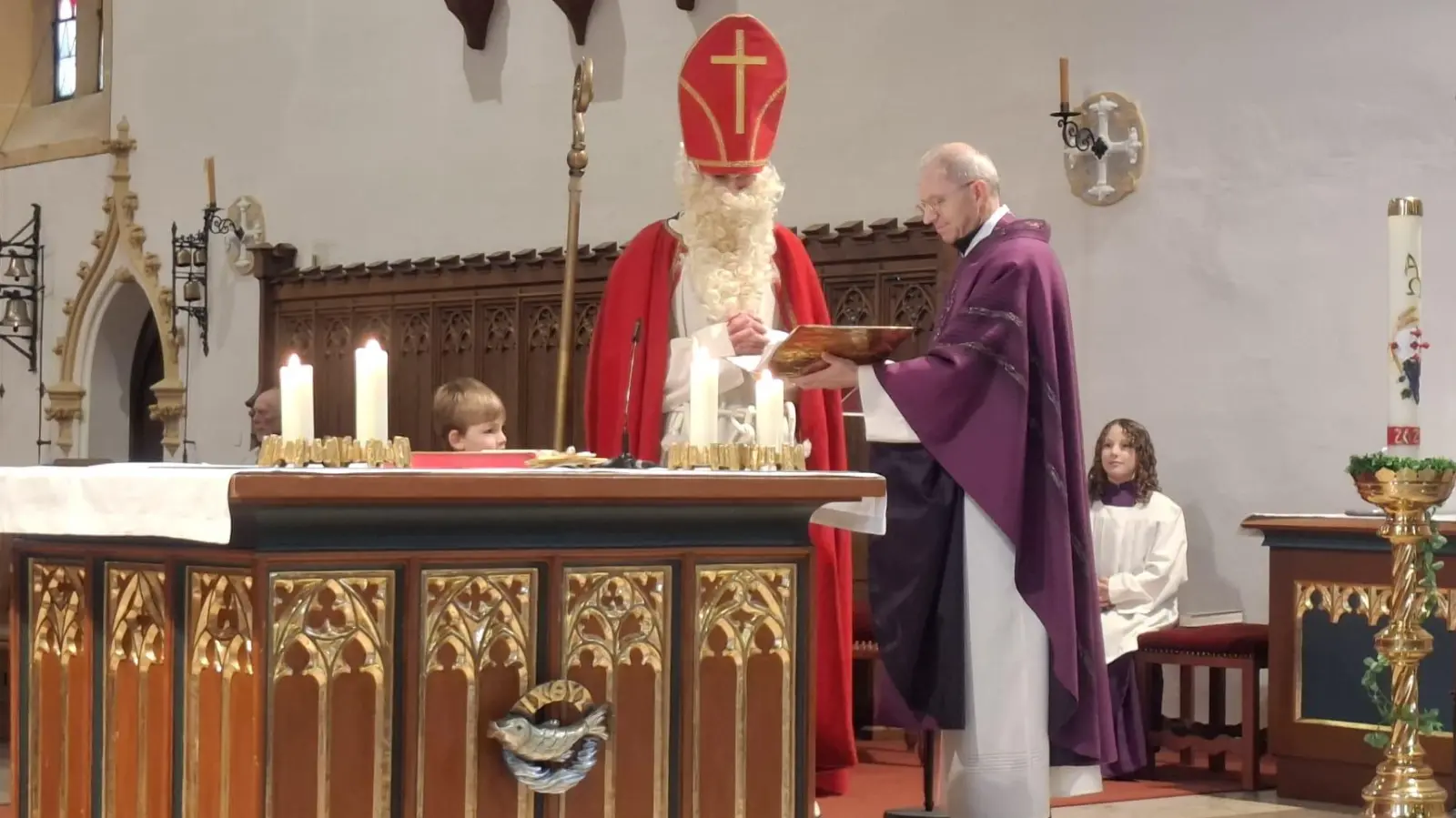 Der heilige Nikolaus liest im Familiengottesdienst aus seinem goldenen Buch, Pfarrer Johann Hofmann und der kleine Benedikt helfen.  (Bild: Lisamarie Schmidl)