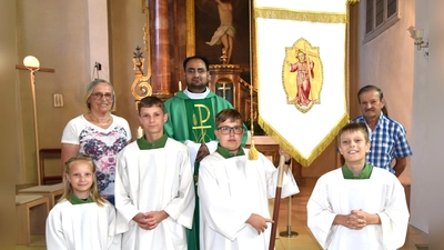 bei der Präsentation der restaurtierten Jugendfahne: (hinten) Mesnerin Elisabeth Dürgner, Pfarrvikar Yeruva und Kirchenpfleger Peter Falk; (vorne) diensthabende Ministranten bei der Sonntagsmesse (Bild: Norbert Weis)