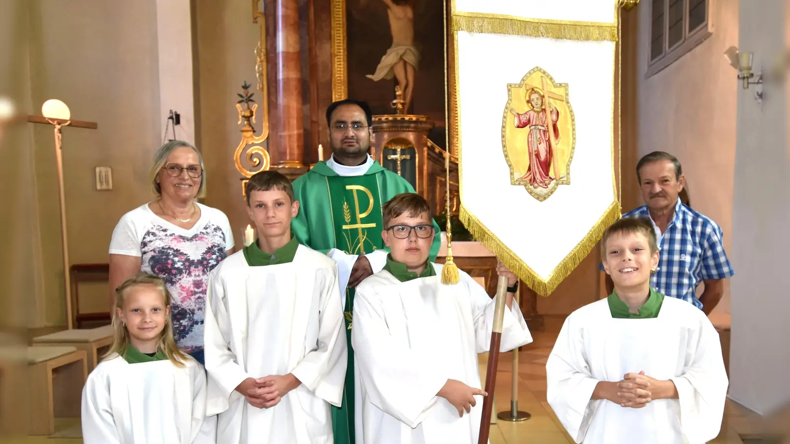 bei der Präsentation der restaurtierten Jugendfahne: (hinten) Mesnerin Elisabeth Dürgner, Pfarrvikar Yeruva und Kirchenpfleger Peter Falk; (vorne) diensthabende Ministranten bei der Sonntagsmesse (Bild: Norbert Weis)