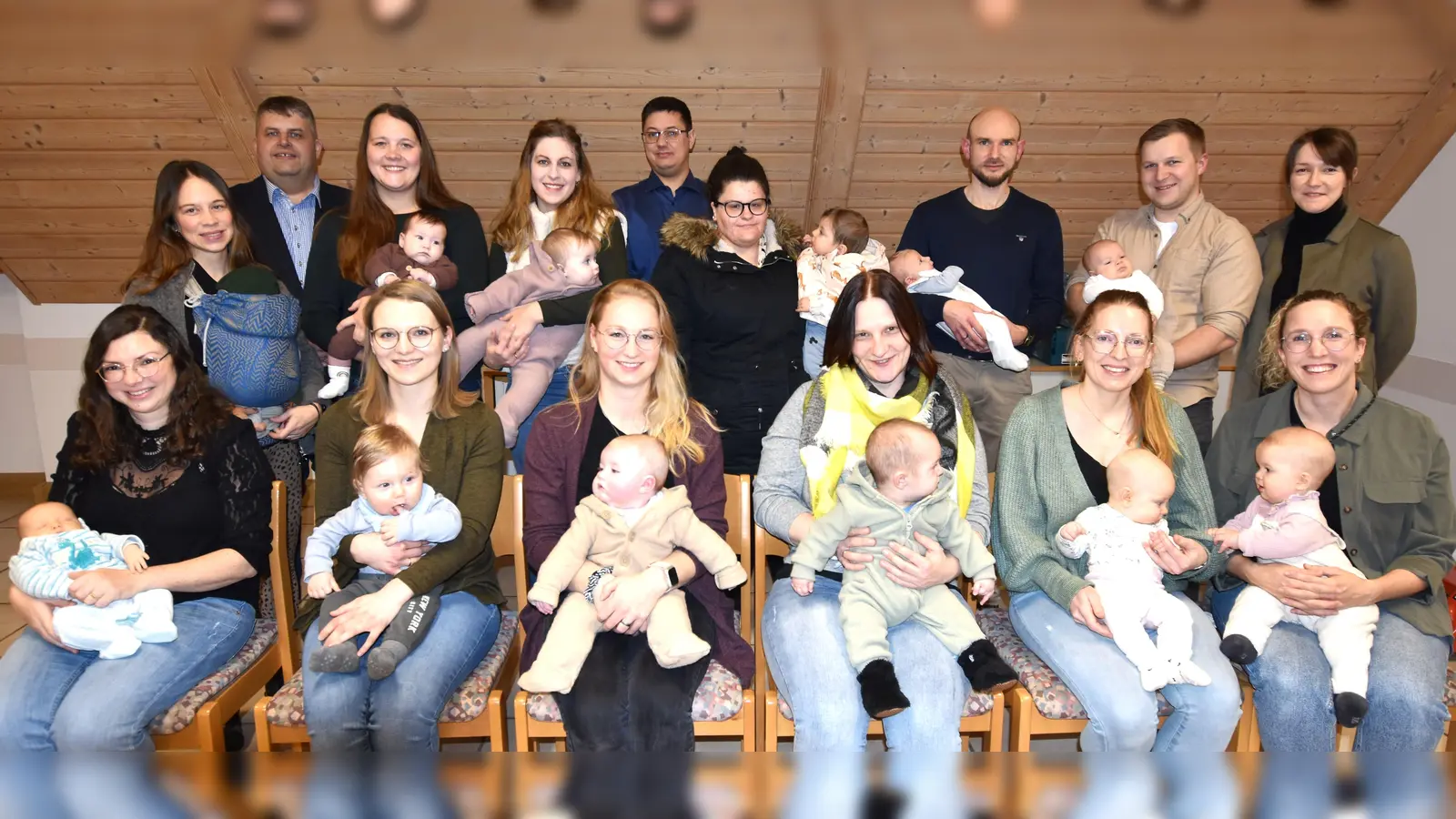 Die Neugeborenen des Jahres 2025 in der Gemeinde Illschwang, mit einem Elternteil, bei der Übergabe des Begrüßungsgeldes durch Bürgermeister Dieter Dehling (stehend /2. von links), 2.Bürgermeister Benjamin Hiltl (stehend/5. von links) und der Jugendbeauftragten im Gemeinderat Selina Englhard (stehend/rechts) im Unterrichtsraum der FF Illschwang (Bild: Norbert Weis)