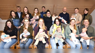 Die Neugeborenen des Jahres 2025 in der Gemeinde Illschwang, mit einem Elternteil, bei der Übergabe des Begrüßungsgeldes durch Bürgermeister Dieter Dehling (stehend /2. von links), 2.Bürgermeister Benjamin Hiltl (stehend/5. von links) und der Jugendbeauftragten im Gemeinderat Selina Englhard (stehend/rechts) im Unterrichtsraum der FF Illschwang (Bild: Norbert Weis)