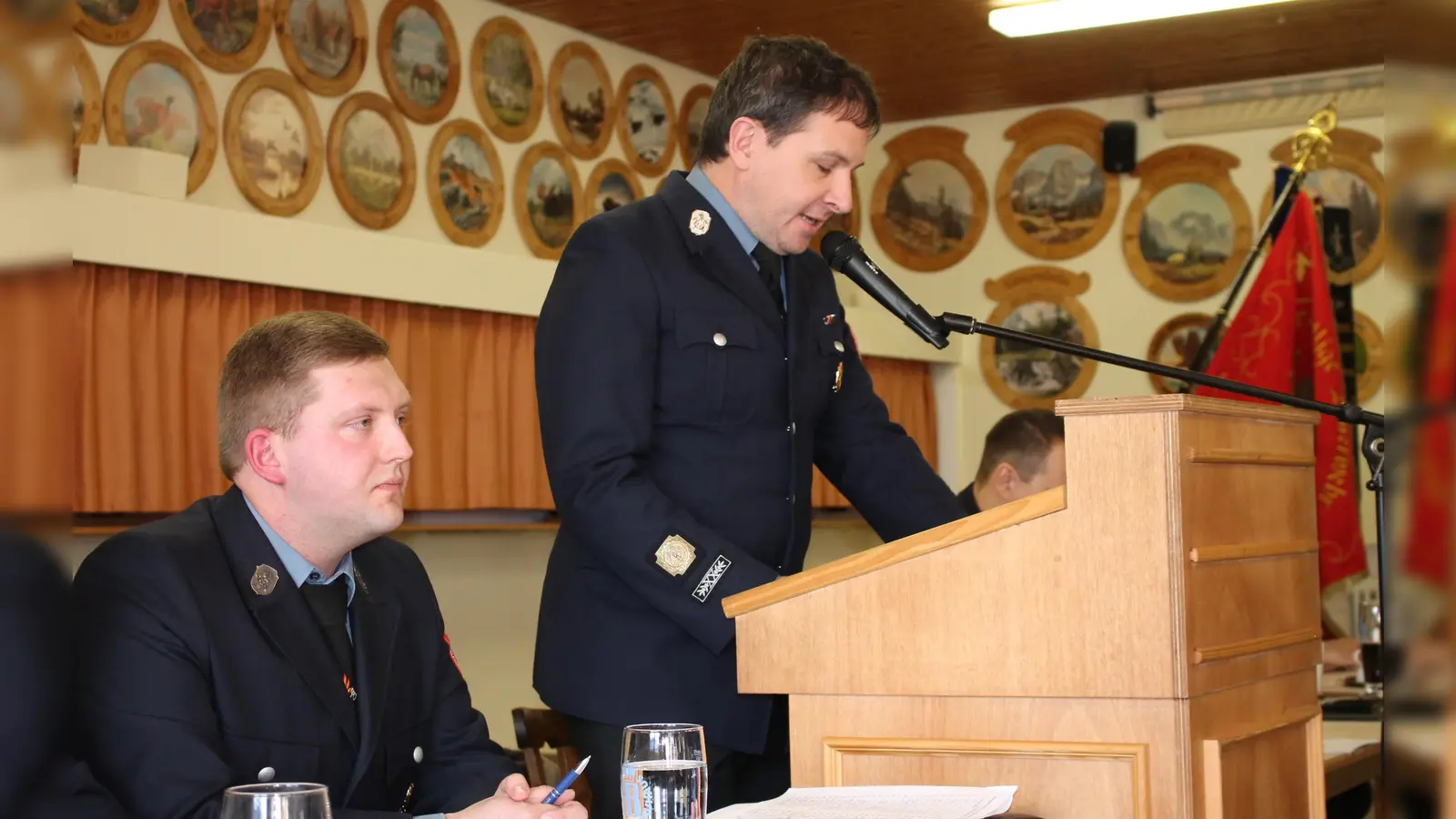 Kommandant Stefan Groß (stehend) und Vorsitzender Johannes Schwemmer blickten bei der Hauptversammlung im Preißacher Schützenheim auf ein an Aktivitäten reiches Jahr der Feuerwehr Burkhardsreuth zurück. (Bild: Bernhard Piegsa)