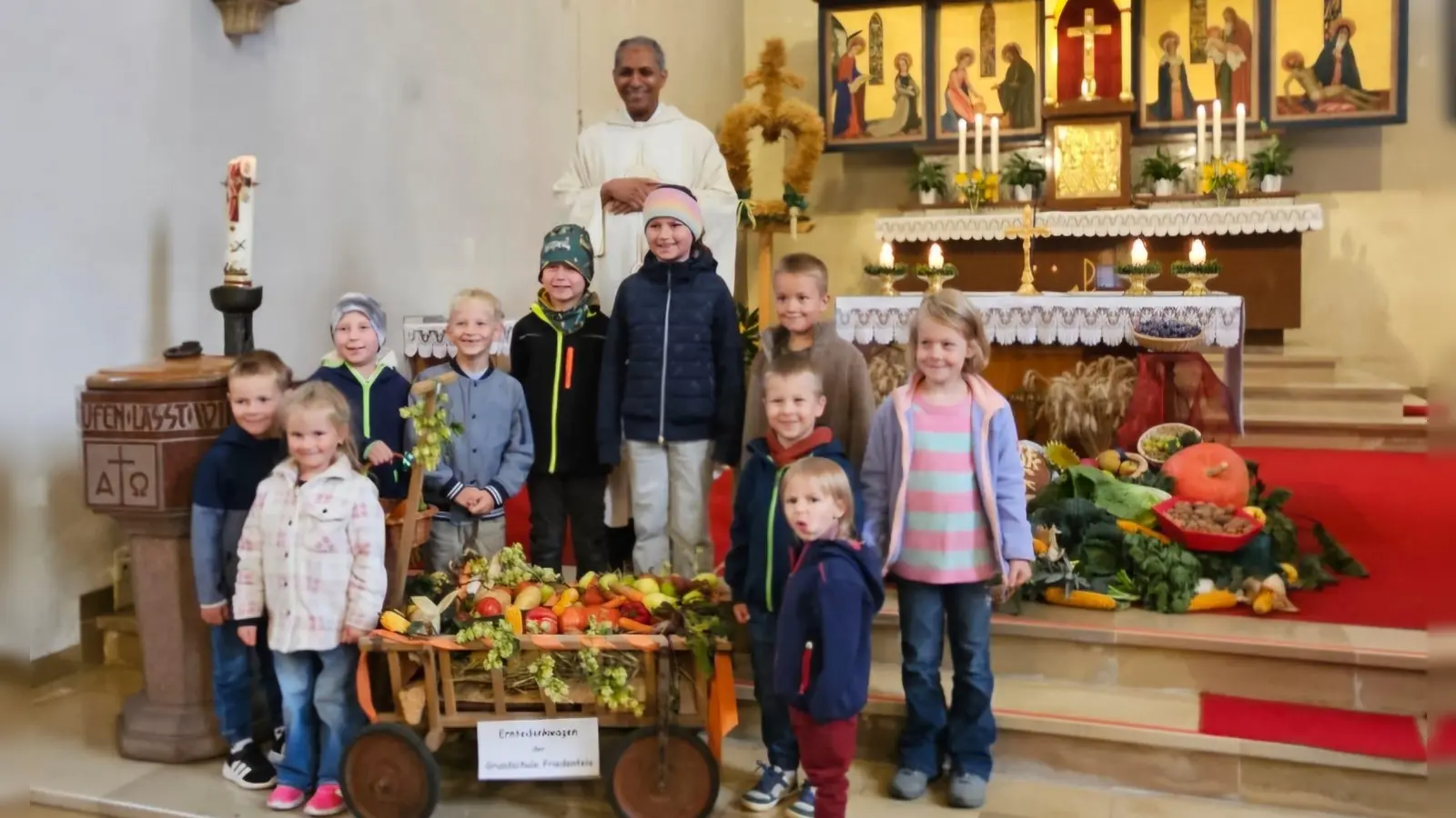 Pater Antony mit einigen Grundschulkindern und ihrem selbst gestalteten Erntedankwagen (Bild: Alexandra Kaßeckert)