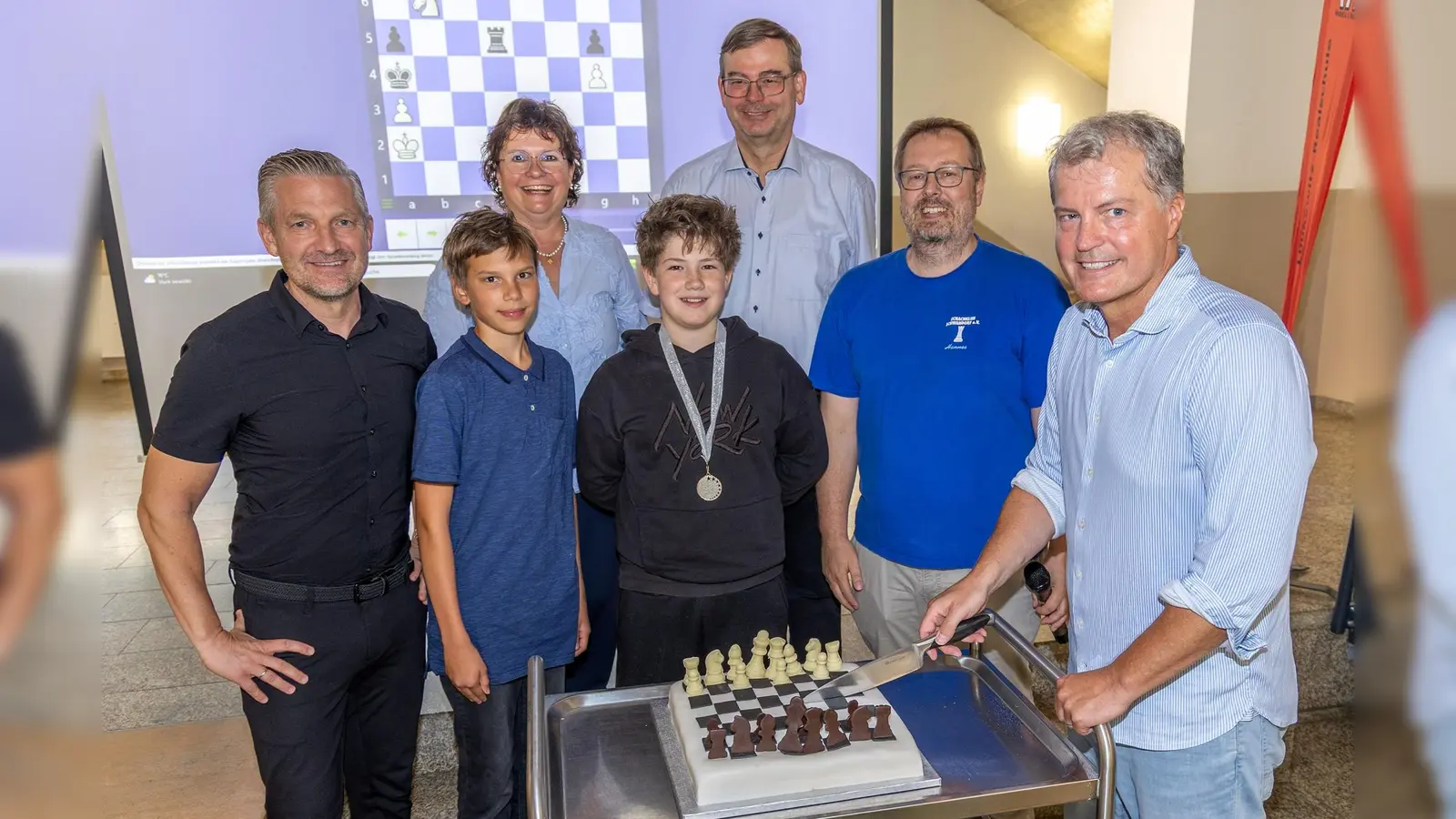 Schachgroßmeister Michael Bezold (vorne rechts) schneidet die Schachtorte an. Außerdem auf dem Bild (v.l.n.r.): Fördervereinsvorsitzender Martin Neuhaus, Konstantin Hüttner, Schulleiterin Irene Sebald, Korbinian Meggenrieder sowie die Schachlehrer Rudolf Lohwasser und Johannes Paar. (Bild: Tobias Neubert)