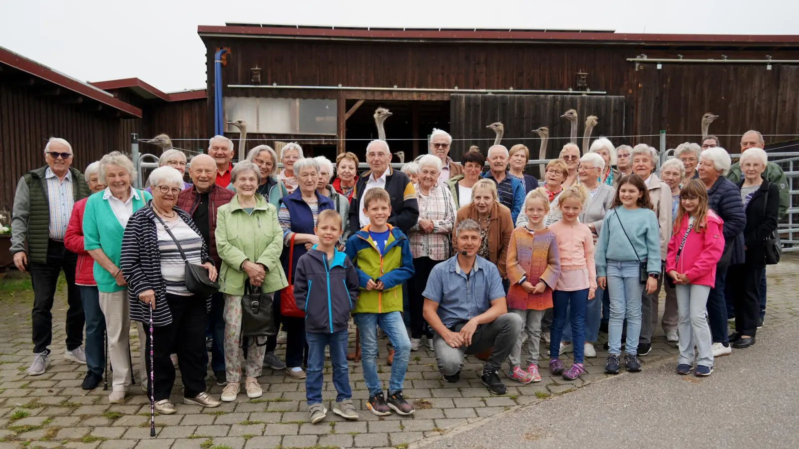 Neugierig beäugt von den Straußen im Hintergrund stellten sich die Besucher für ein Gruppenfoto auf. (Bild: Alois Schröpf)