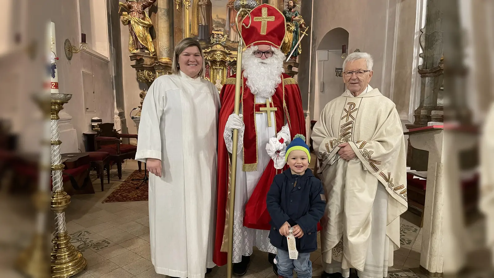 Im Erinnerungsbild (von links) Gemeindereferentin Kathrin Blödt, der Heilige vom Himmel, dann der Bub Vinzenz, der sichtlich keinerlei Angst vor dem Himmelsmann hatte und Pfarrer Josef Beer. Der Nikolaus sprach von viel Not unter den Menschen seiner Zeit, wie beispielweise den Armen und wie er ihnen in seiner Güte mit heimlichen Gaben geholfen habe. <br> (Bild: Michael Götz)