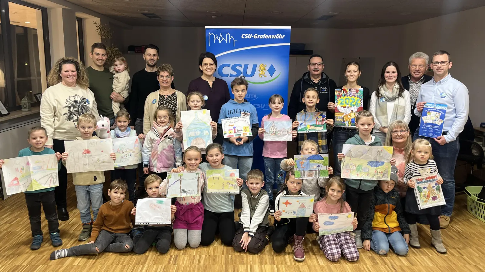 Stolz präsentierten die Kinder ihre Bilder auf denen Sie ihre Wünsche und Ideen für ihr Grafenwöhr der Zukunft auf Papier brachten. 12 Motive sind im CSU-FU-JU Kalender des Jahres 2026 nun zu finden. Die Stadtratskandidaten der CSU gratulierten den jungen Künstlern.  (Bild: Julia Brunner )