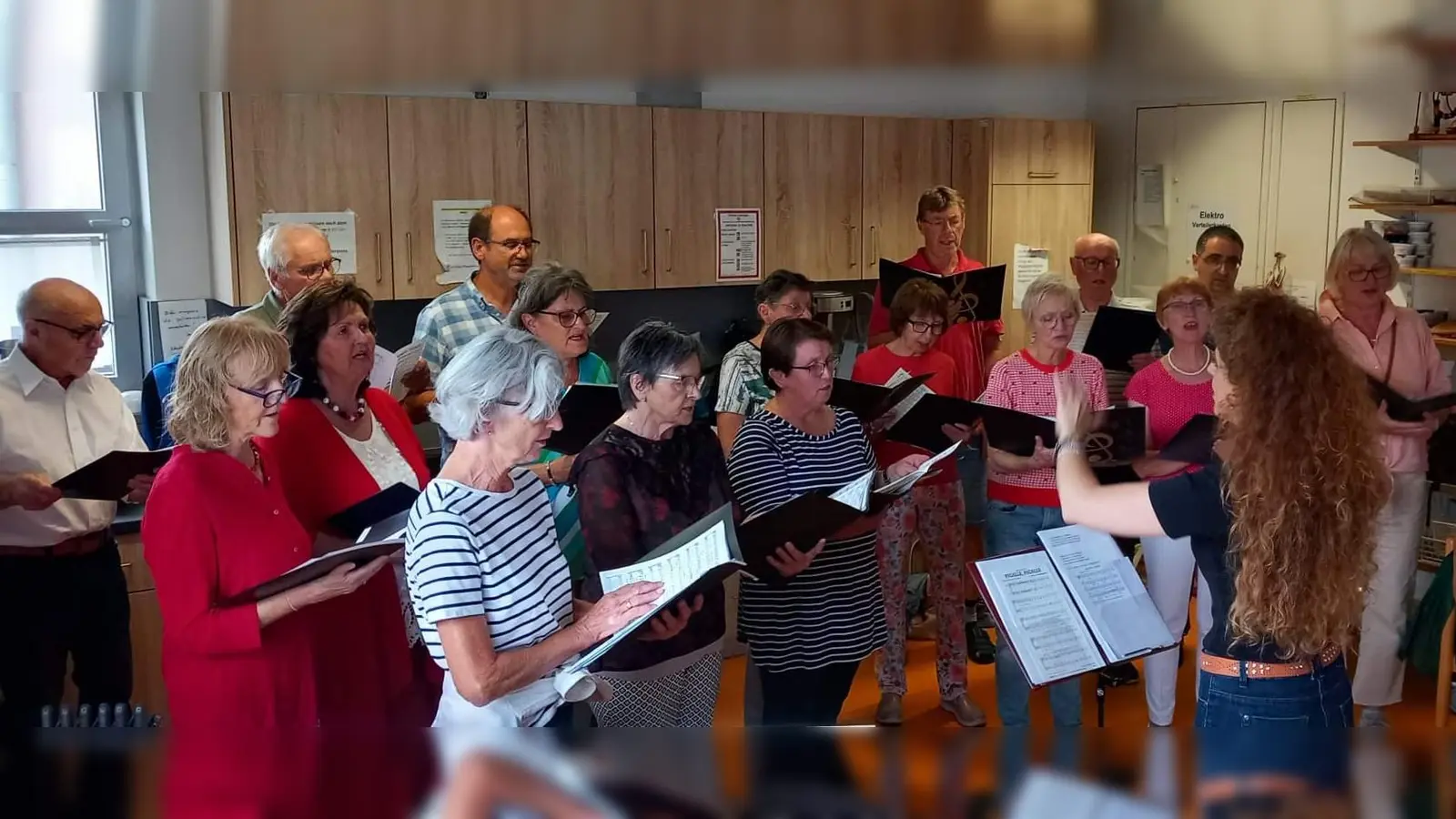 Mit seiner Serenade, die wegen des Wetters vom Garten ins Heim verlegt wurde, bereitete der Gemischte Chor unter Leitung von Jana Müller (am Dirigentenpult) den Bewohnern des BRK Seniorenwohn- und Pflegeheims St. Barbara und den Gästen einen stimmungsvollen und kurzweiligen Abend. Sitzend die Vorsitzende Renée Ehringer-Hoffmann. (Bild: Werner Schulz)