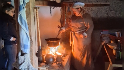 Michaela Hahn, Gastgeberin und Köchin, steht mit Teilnehmern an der Feuerstelle im Bauernhaus und kocht (Bild: Antje Grüner)