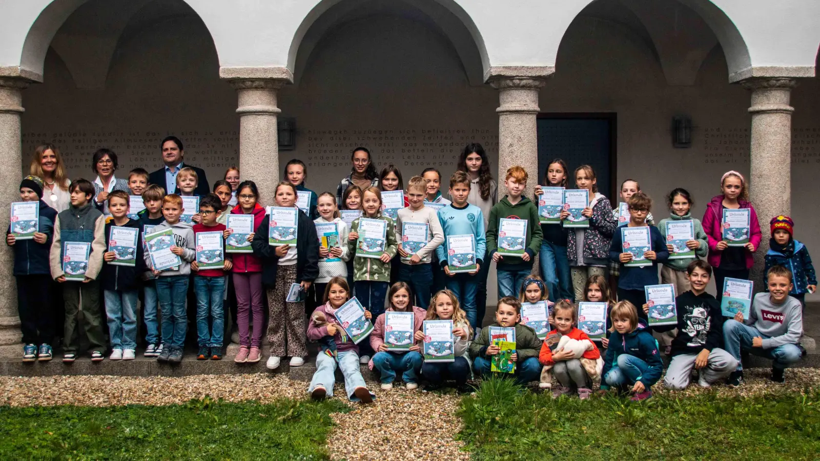 Am Sommerferien-Leseclub 2026 teilnehmende Kinder mit ihren Urkunden. Im Hintergrund Kinderbuchautorin Anna Ludwig, 1. Bürgermeister Florian Reger und Büchereileiterin Irmi Sittl. (Bild: Kurt F. Stangl)