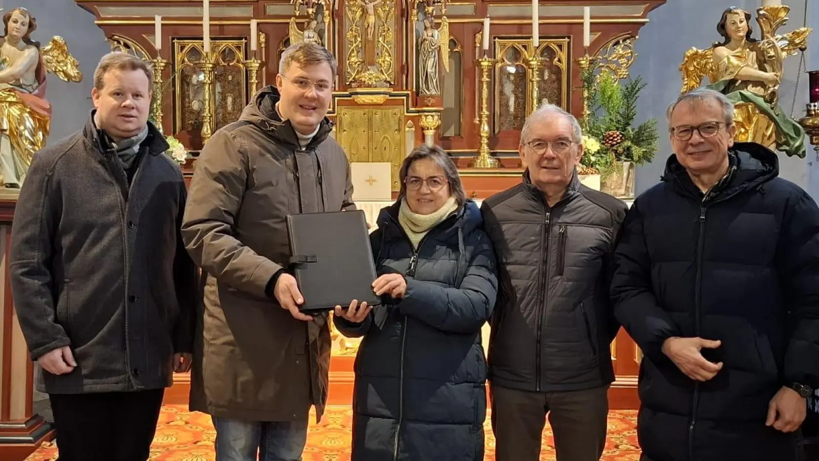 Das Bild zeigt die Übergabe einer Geldspende in einer Chormappe durch Frieda Zeitler an Chorleiter Christian Kipfelsberger Personen v.l.n.r.: Pfarrer Thomas Kraus, Chorleiter Christian Kipfelsberger, Chormitglied Frieda Zeitler, Ehrenchorleiter Albert Schraml, Kirchenpfleger Michael Braunreuther (Bild: Birgit Übelmesser)