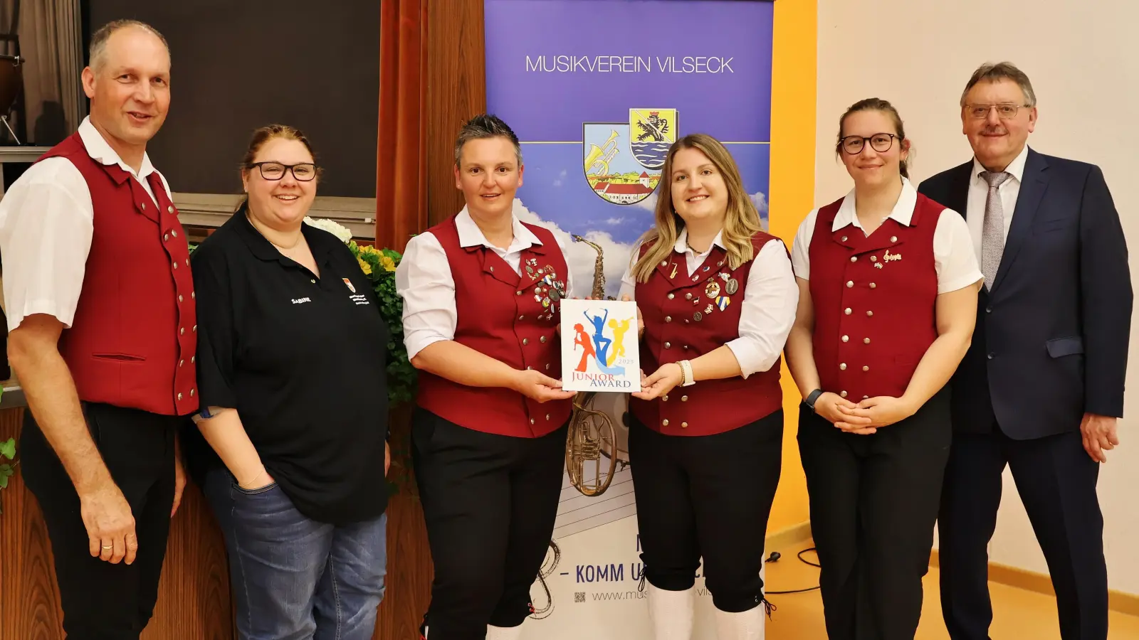 Mit großer Freude und Stolz können die Mitglieder der Vorstandschaft den neu verliehenen „Junior Award“ präsentieren. v.l.n.r. Vorsitzender Christian Winklmann, Sabine Kredler von NBMB, Notenwartin Isabella Rauscher, Jugendleiterin Maria Siegler, Dirigentin Wanda Gardner und Bürgermeister Hans-Martin Schertl (Bild: Isabella Rauscher)