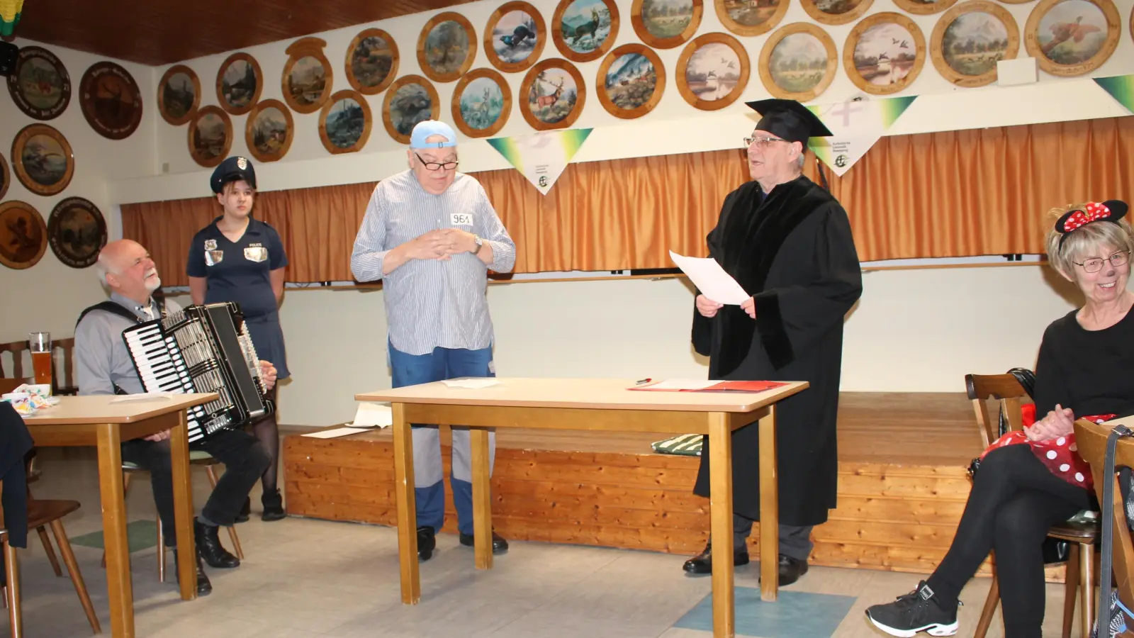 Delinquent Pimplmoser (Hans Hofmann, Dritter von links) blickte betreten drein. als ihn der „Richter” (Dieter Klein, Vierter von links) zu vier Jahren verdonnerte. Da hatte es auch nichts genützt, dass der „Angeklagte” geltend gemacht hatte, sein One-Night-Stand Rosemarie habe ihn mit den zufriedenen Worten „Junge, komm bald wieder” verabschiedet. Links Musiker Gerhard Retzer, rechts Gisela Rodler. (Bild: Bernhard Piegsa)