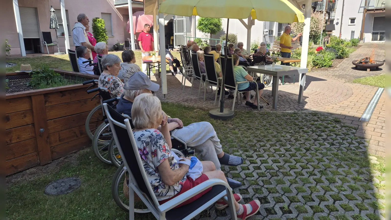 In einem besonderen Rahmen, nämlich verbunden mit einem Johannisfeuer, fand die Bewohnerversammlung des BRK-Seniorenheims St. Barbara statt. Nach dem Bericht des Beiratsvorsitzender Rudi Wild (stehend rechts) segnete Stadtpfarrer Johann Hofmann das Johannisfeuer. Rechts neben ihm (halb verdeckt). Heimleiterin Astrid Geitner. (Bild: Anita Dobmeier)