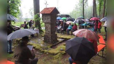 (links) Michael Koller fungiert als Schirmträger für Diakon Eiber. Die Besucher feierten andächtig mit. Ein Teil der Grundmauer der Kapelle konnte erhalten werden, in der Mitte der Bildstock. (Bild:  Ludwig Krauß)