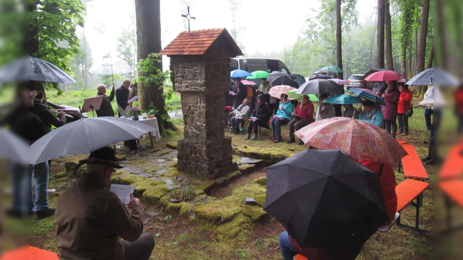 (links) Michael Koller fungiert als Schirmträger für Diakon Eiber. Die Besucher feierten andächtig mit. Ein Teil der Grundmauer der Kapelle konnte erhalten werden, in der Mitte der Bildstock. (Bild:  Ludwig Krauß)