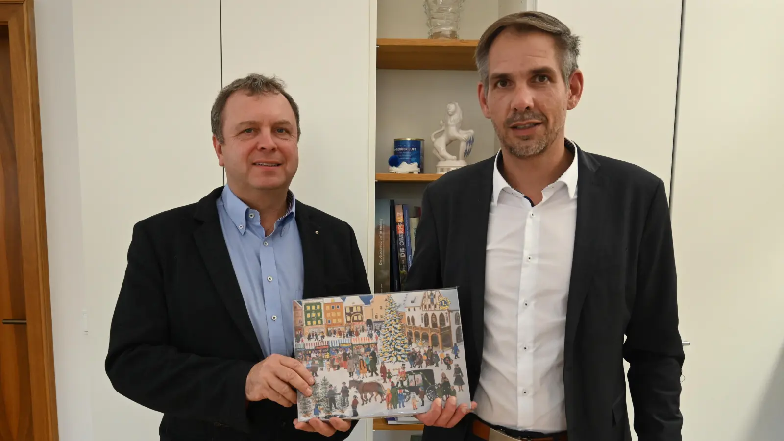 Oberbürgermeister Michael Fritz (rechts) erhält den ersten Lions-Adventskalender 2026 von Andreas Herrmann (links), Vorsitzender des Lions-Hilfswerks.  (Bild: Simon Hauck)