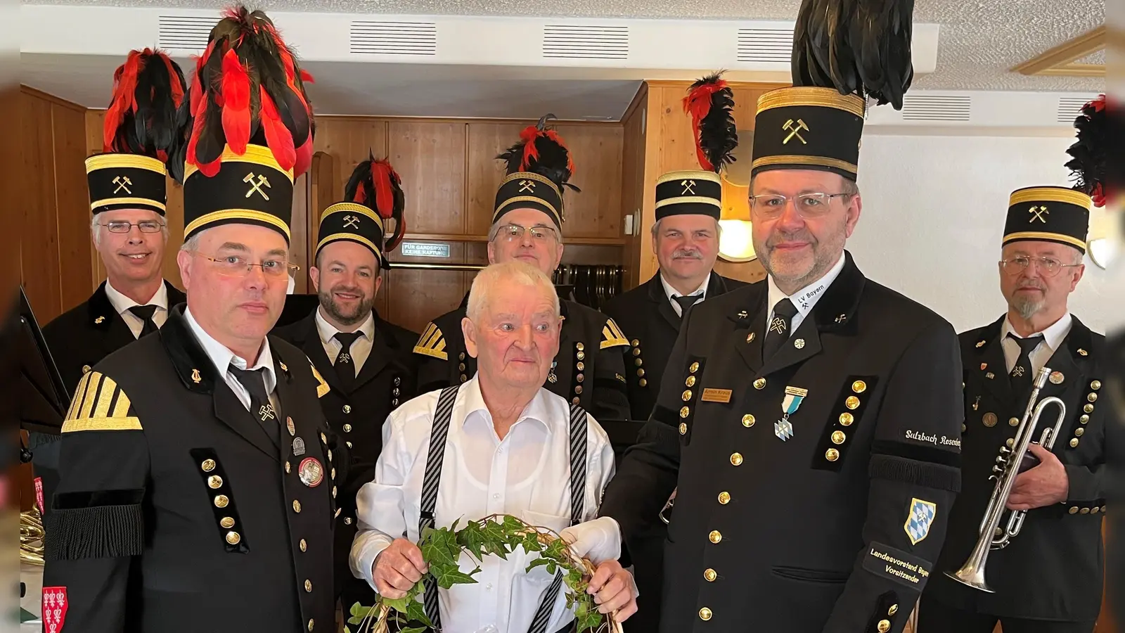 v.l. 2.Vorstand Martin Kernl, Jubilar Richard „Pömerer” Fuchs und 1.Vorstand Armin Kraus gratulierten mit einem Geschenkkorb. Im Hintergrund eine Abordnung der Bergknappenkapelle unter der Leitung von Siegfried Meier (hi.Mitte). (Bild: Karin Kraus)
