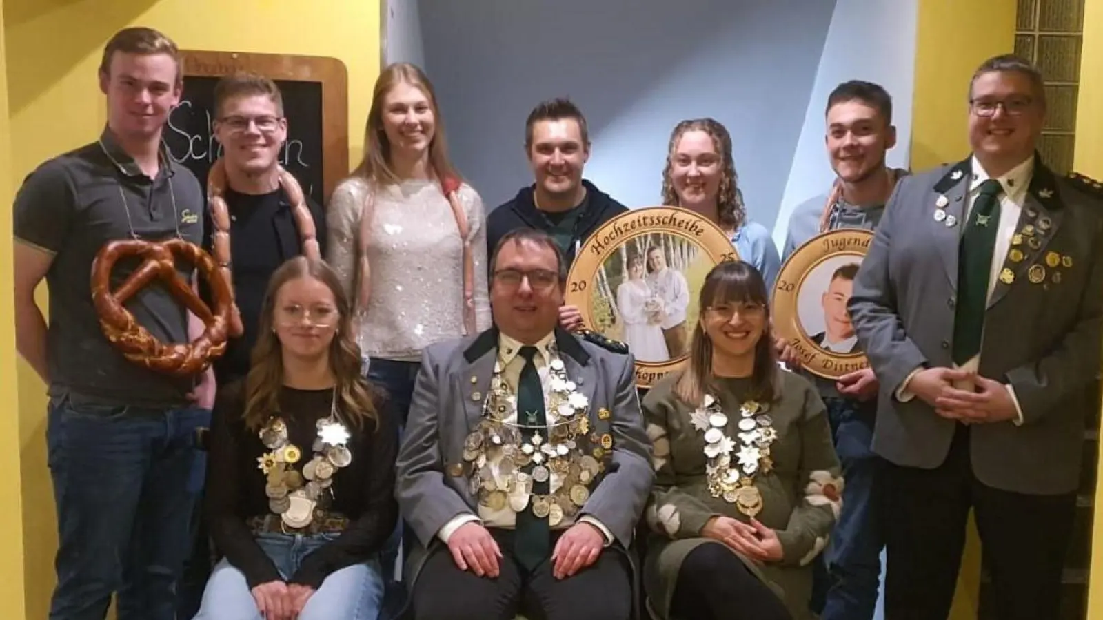 Schützenmeister Dominik Brenner (stehend, Erster von rechts) gratulierte Jugendkönigin Laura Brenner, Schützenkönig Florian Frischmann und Schützenliesl Carina Schopper (vorne sitzend von links nach rechts) zur jeweiligen Königswürde, sowie Maria Distner (stehend, Dritte von rechts) zum Gewinn der Hochzeitsscheibe von Carina und Andreas Schopper. (Bild: Peter Kirner)