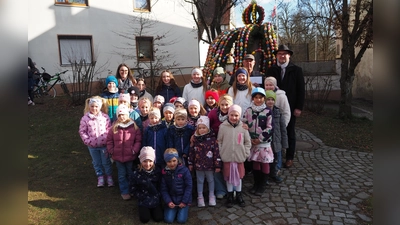 Mit Liedbeiträgen vor dem Osterbrunnen erfreute die Pfiffikusbande alle Anwesenden. Bürgermeister Richard Kammerer (hinten rechts) überreichte an Georg Seiser (hinten links) eine Geldspende. (Bild: Johann Kneißl )