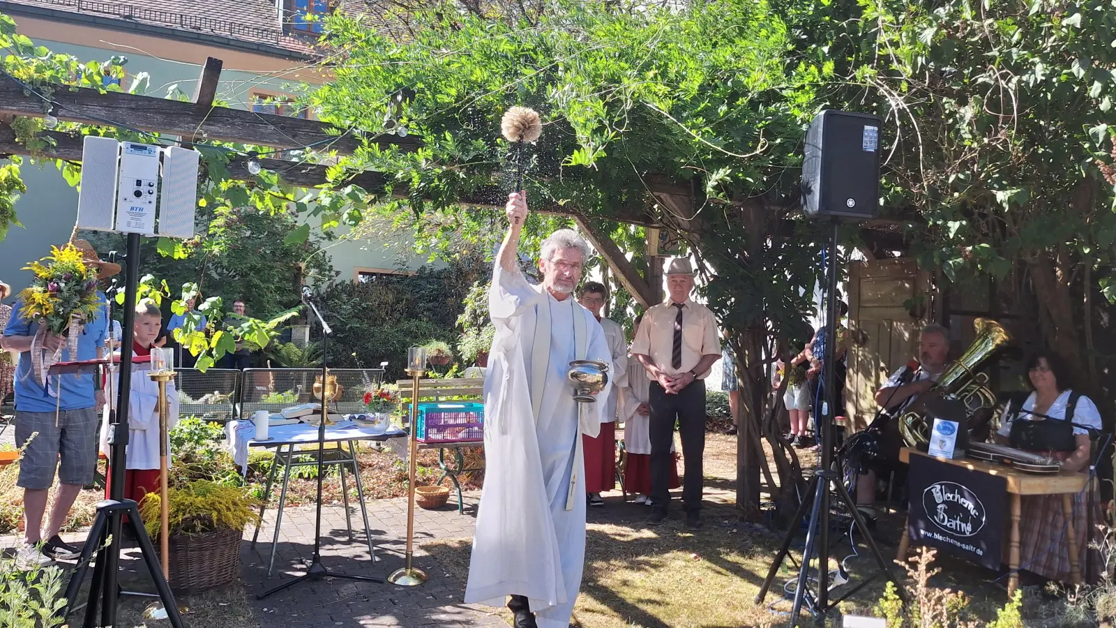 Pfarrer Brügel bei der Kräutersegnung im Kräutergarten. Rechts im Bild die „Blechernen Saitn”, die den Gottesdienst musikalisch umrahmten. (Bild: Anita Hartmann)