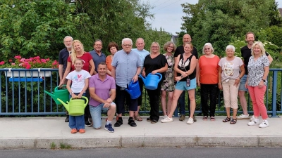 Insgesamt acht Blumenkästen wurden an der Mühlbachbrücke wieder angebracht. Auf dem Bild ein Teil der Anwohner, die den Blumenschmuck pflegen. Uwe Bergmann (vorne, Zweiter von links) und Harald Kausler (Zweiter von rechts) hatten das Ganze wieder organisiert. Zweite Bürgermeisterin Elisabeth Kraus (rechts) lud im Namen der Stadt zu einem kleinen Umtrunk ein. (Bild: David Bergmann)