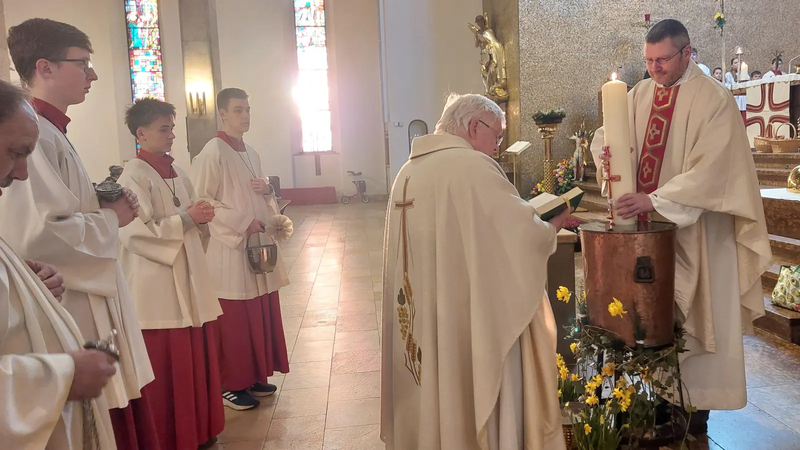 Stadtpfarrer Gottfried Schubach und Pfarrvikar Reinold Bogensperger tauchen die Osterkerze ins Weihwasserbecken.  (Bild: Helmut Kunz)