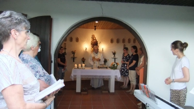 Ruhestandspfarrer Josef Beer steht am Altar des hell erleuchteten Kirchleins, im Hintergrund die Madonna der Gottesmutter. Links Chorsängerinnen, rechts Karin Hottner vor der Orgel. Die Marienkapelle in Diebis sieht man gut von der vorbeiführenden Staatstraße aus.  (Bild: Michael Götz)