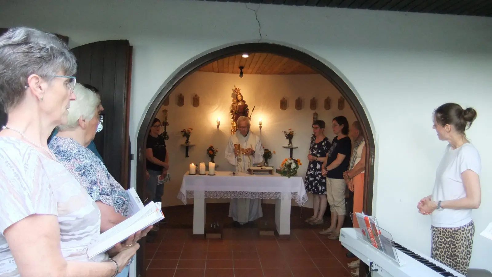 Ruhestandspfarrer Josef Beer steht am Altar des hell erleuchteten Kirchleins, im Hintergrund die Madonna der Gottesmutter. Links Chorsängerinnen, rechts Karin Hottner vor der Orgel. Die Marienkapelle in Diebis sieht man gut von der vorbeiführenden Staatstraße aus.  (Bild: Michael Götz)