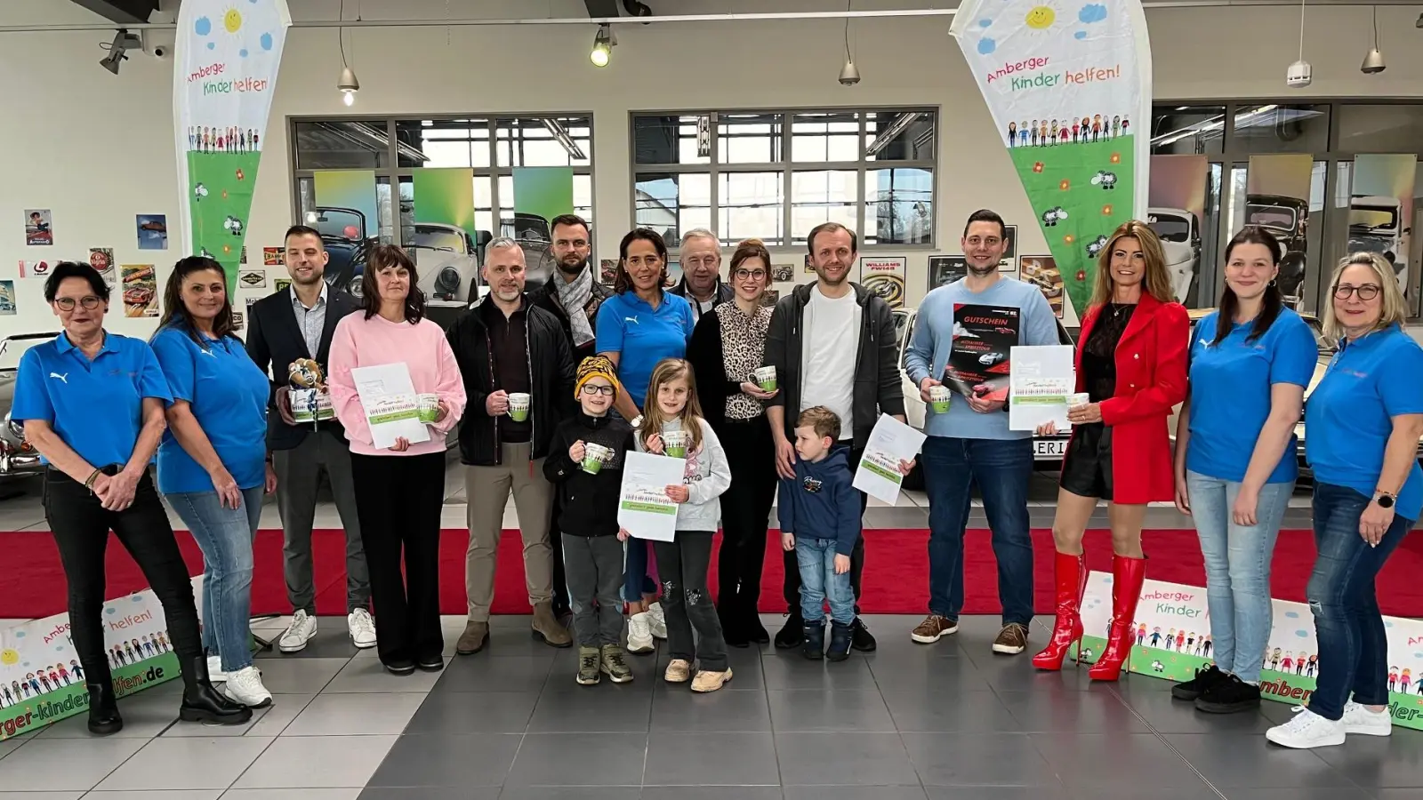 Vorsitzende Anne Wagner (Bildmitte mit blauem Polohemd) freute sich, in der Wagner-Oldtimer-Galerie zusammen mit ihren Vereinsmitgliedern (alle in blauen T-Shirts) viele „Motorwelten”-Preise an die Gewinner übergeben zu können; das Bild zeigt von links Michaela Sperl, Nevin Yerlikaya, Dominik Obermeier (O.S.A.), Gabi Farnbauer, Alexander Granberg (Auto Fischer), Mateusz Osicki (O.S.A.), Anne Wagner, Winfried Osicki (O.S.A.), Selina und Alexander Riemer, Thomas Gräml, Sandra Winter (Bausanierung-BZ) und ganz rechts Kirsten Prax. (Bild: Thomas Amann)